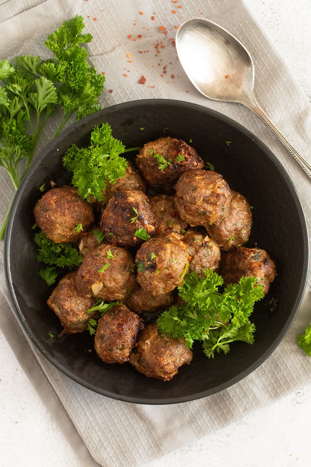 many small meatballs and fresh parsley in a black bowl.