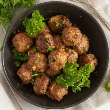 meatballs without breadcrumbs and fresh parsley sprigs in a small bowl.