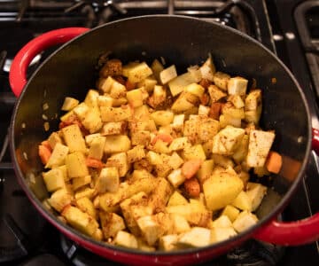 mixing root vegetables with spices in a soup pot.