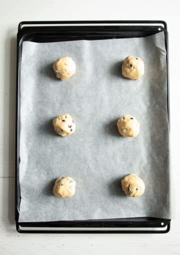 six bowls of cookie dough on a baking sheet lined with parchment paper.