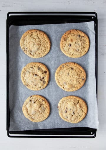 six freshly baked cookies on a baking tray lined wit parchment paper.