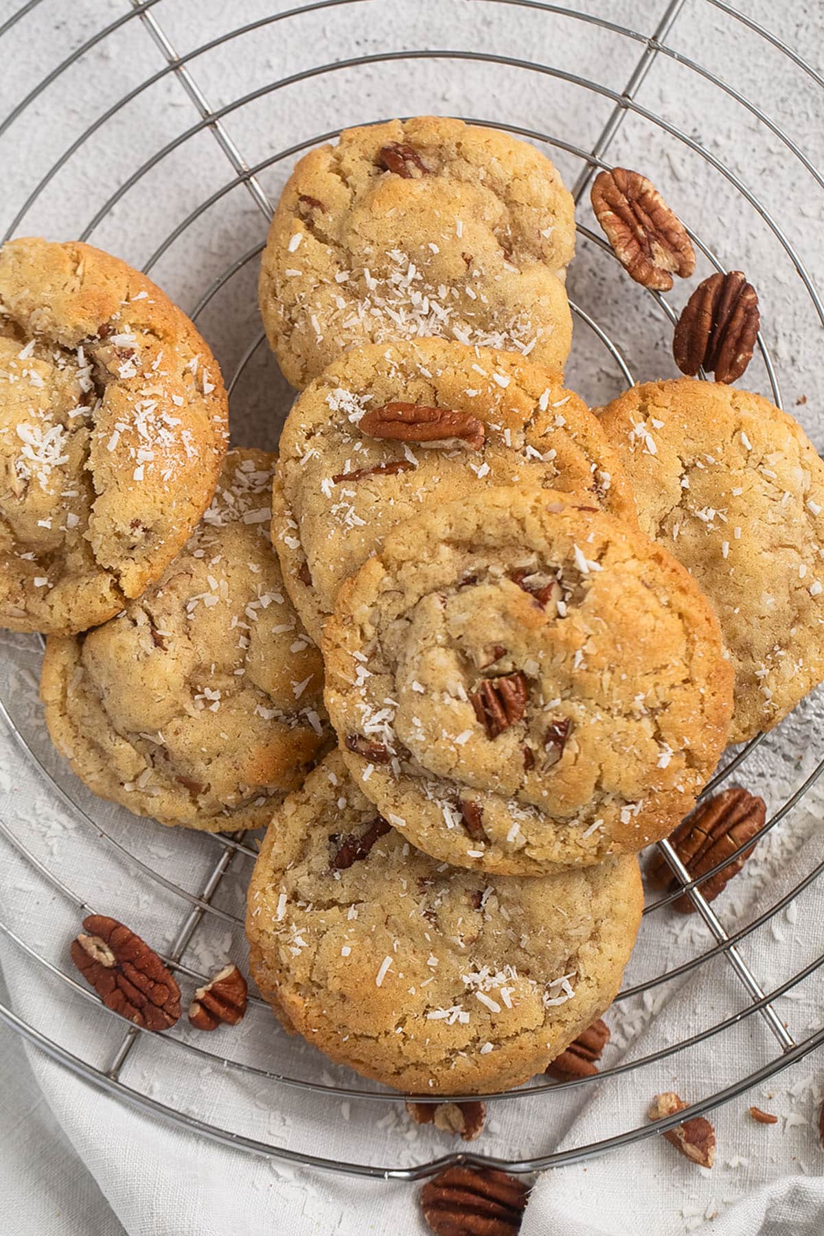 many pecan and coconut cookies on a wire rack, pecans scattered around it.