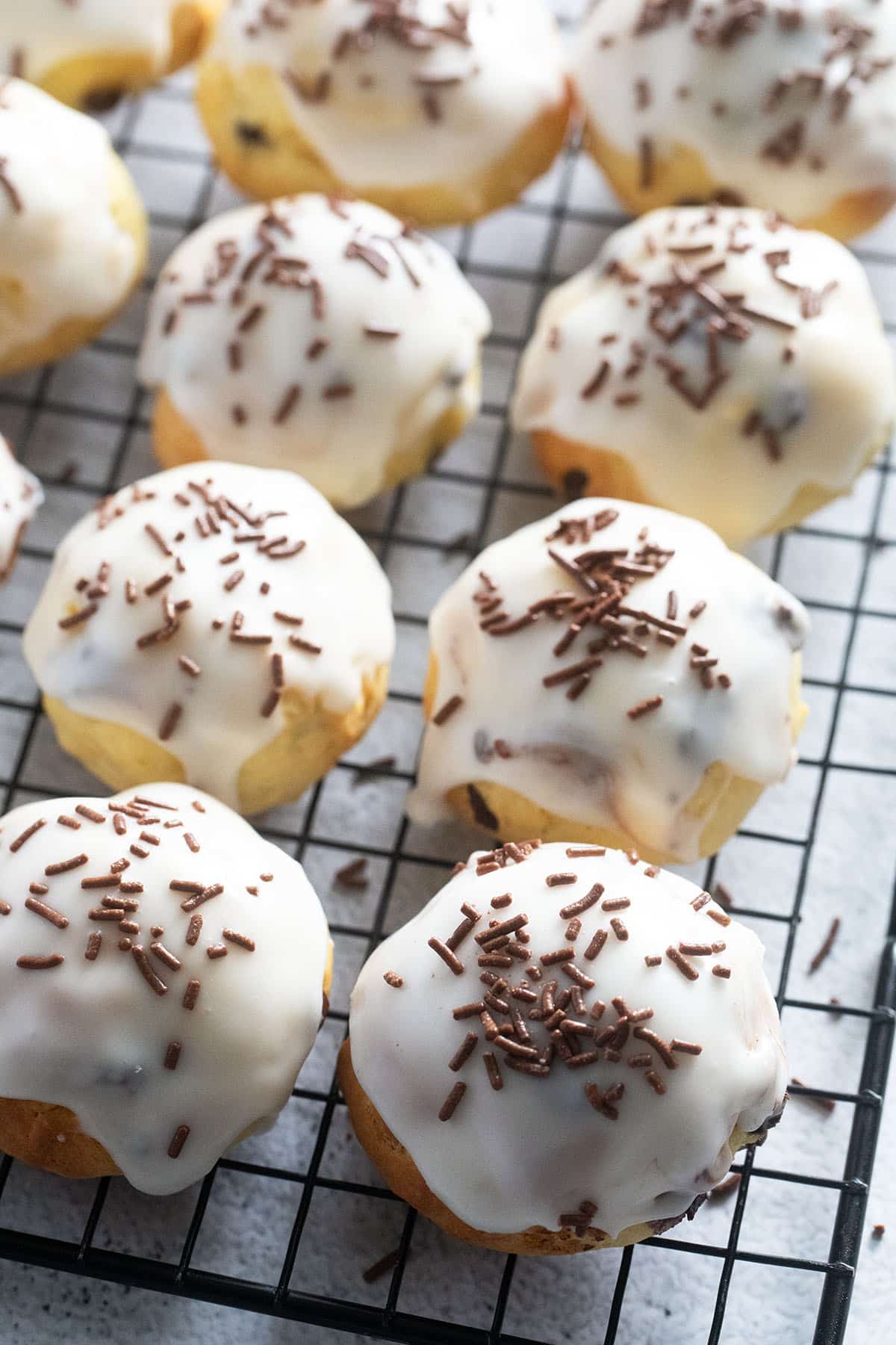 many glazed ricotta cookies sprinkled with chocolate on a wire rack.