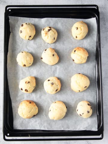 twelve ricotta cookies with chocolate chips on a baking tray.