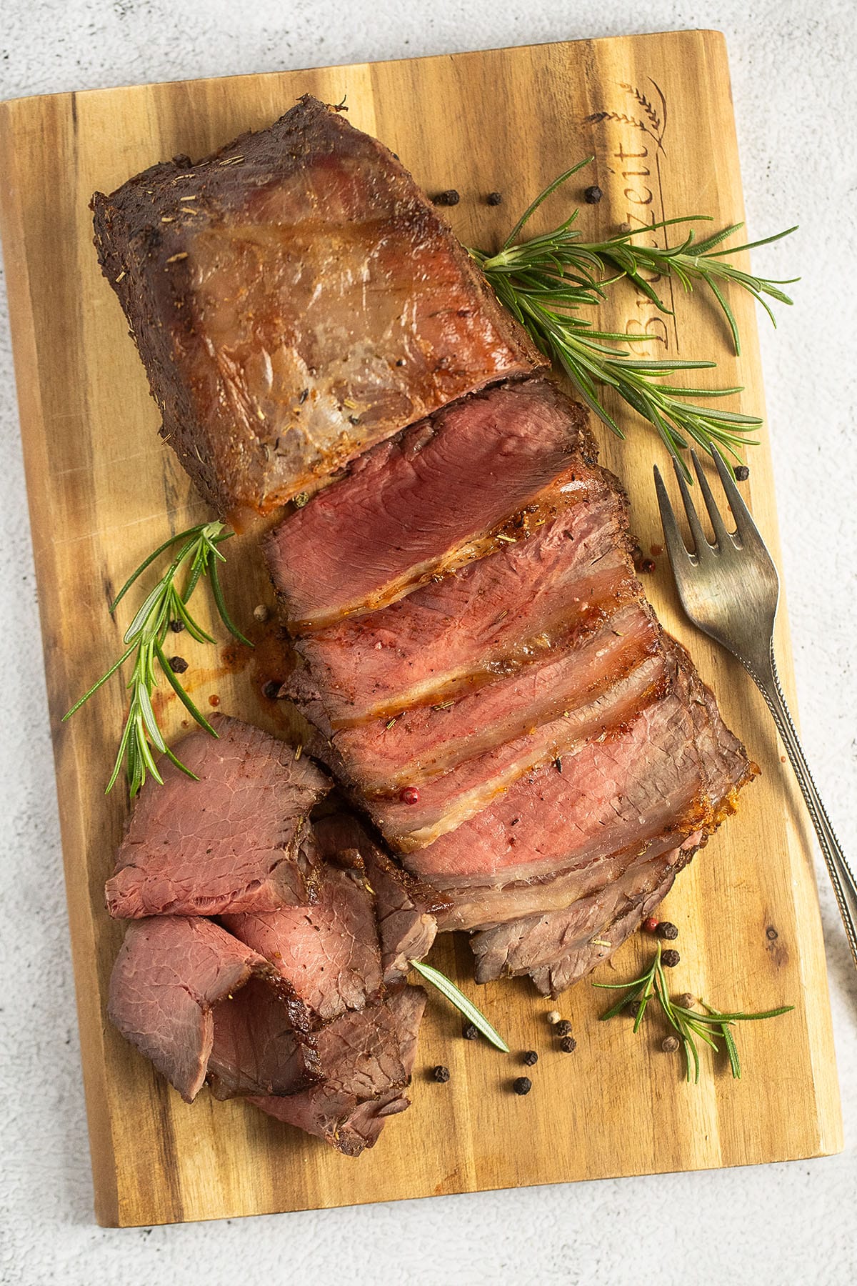 cold sliced beef on a cutting board with rosemary sprigs around it.