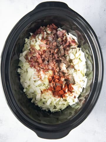 mixing raw chopped cabbage with bacon and spices in the pot of a crockpot.