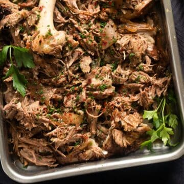pulled lamb and sprigs of parsley in a roasting tin.