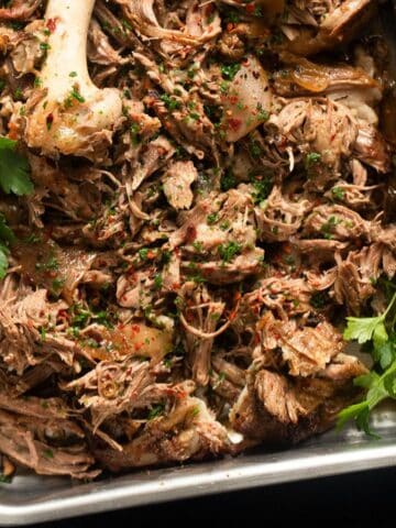 pulled lamb and sprigs of parsley in a roasting tin.