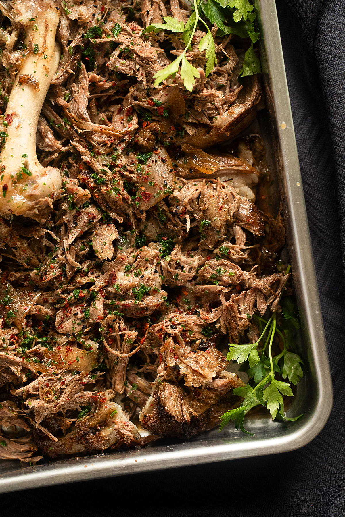 pulled lamb shoulder pieces in a roasting tin with parsley.