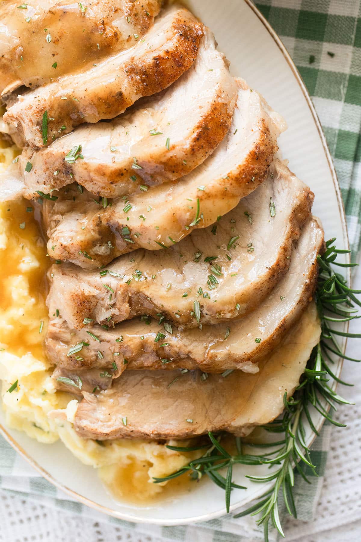 sliced pork loin with mashed potatoes and rosemary sprigs on a platter.