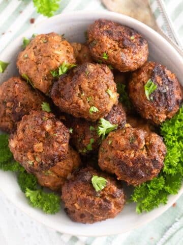 many small meatballs without eggs in a bowl with fresh parsley around them.