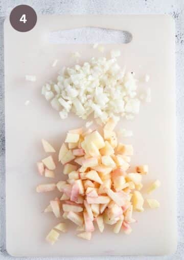 chopped peeled apples and onions on a white cutting board.