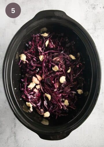 raw shredded red cabbage dotted with butter pieces in the pot of a slow cooker.