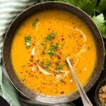 lovage soup sprinkled with chopped herbs, cream and red pepper flakes in a bowl.