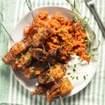 two pork belly skewers served with rice and yogurt on a plate.
