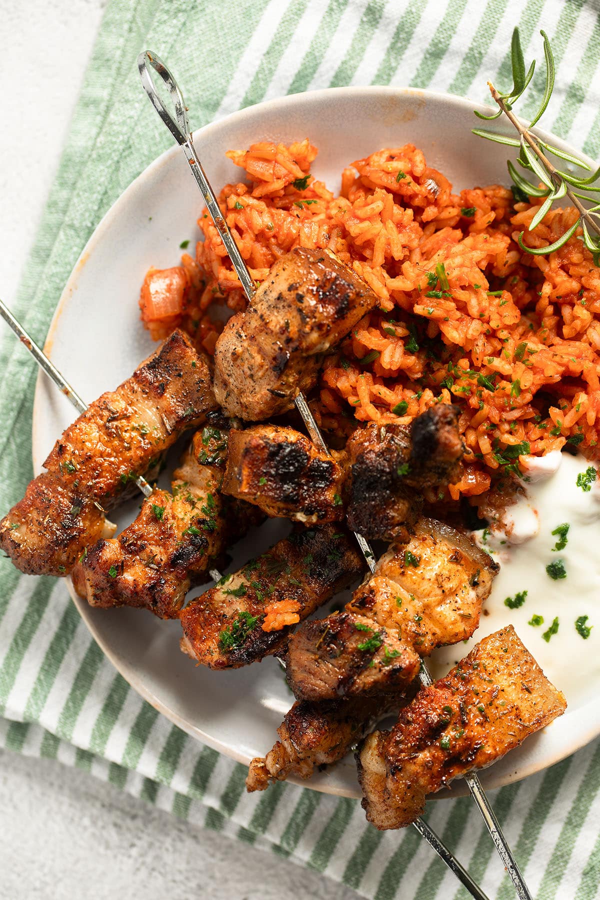 pork belly skewers with greek rice on a plate.