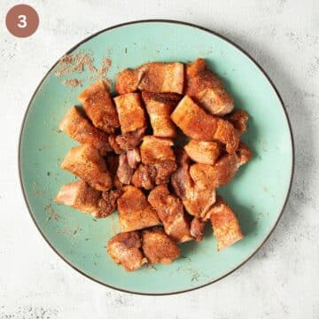 pork belly cubes tossed with seasoning on a large plate.