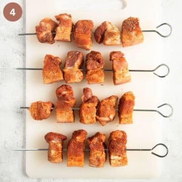 four skewers, each one with four pieces of raw and seasoned pork cubes.