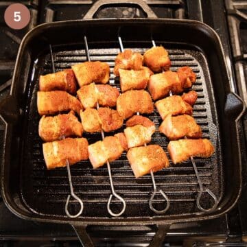 four skewers with raw pork cubes in a grill pan.