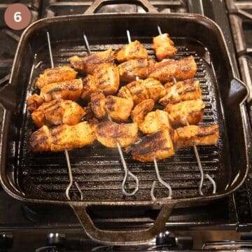 four skewers with pork belly cooking in a grill pan.