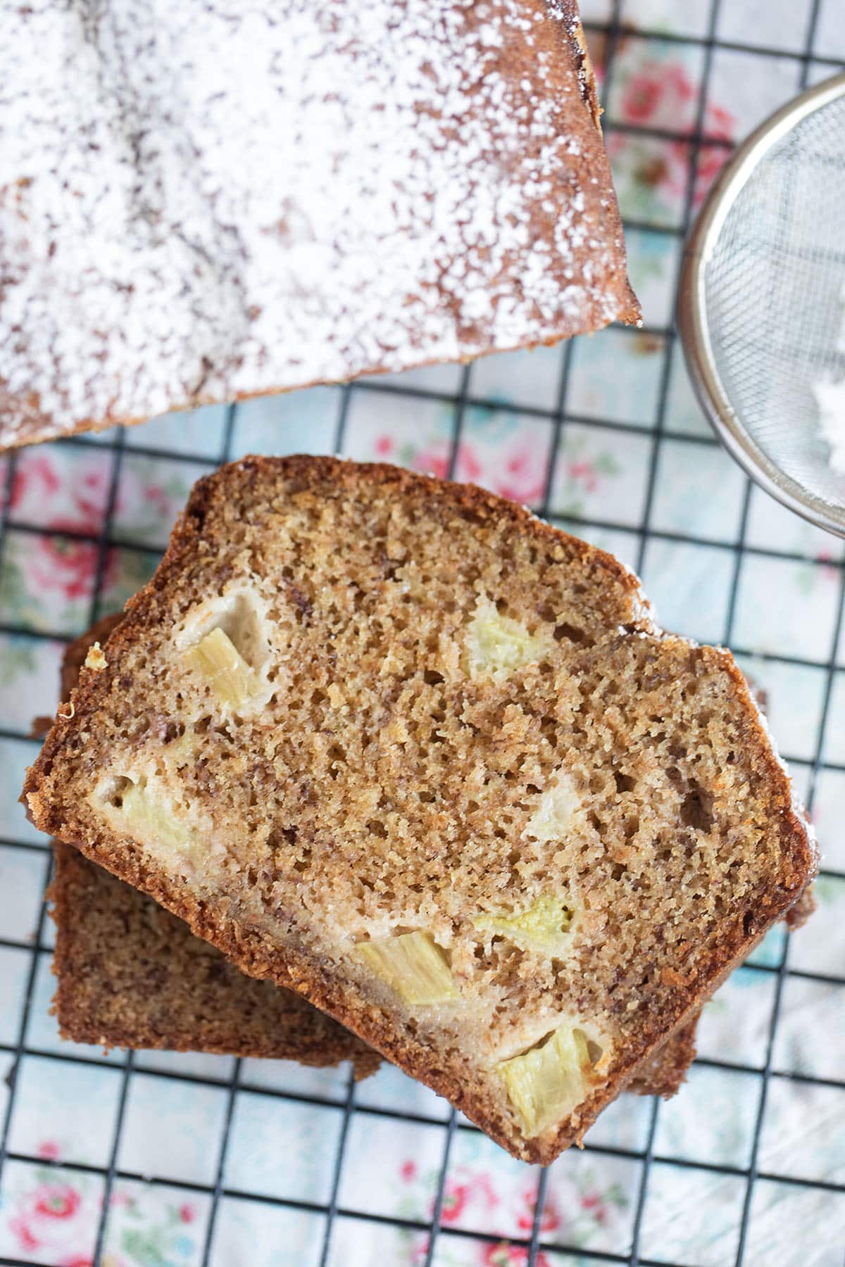 two slices of banana bread with rhubarb on top of each other and the rest of the loaf near it.