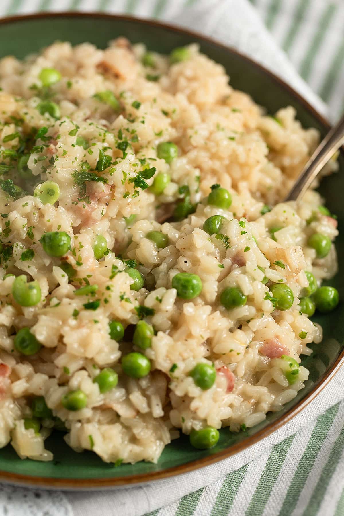 a full plate with risotto with peas and bacon with a fork in it.