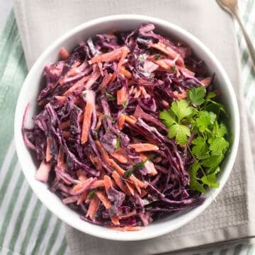 purple cabbage and carrot slaw with parsley and creamy dressing in a bowl.