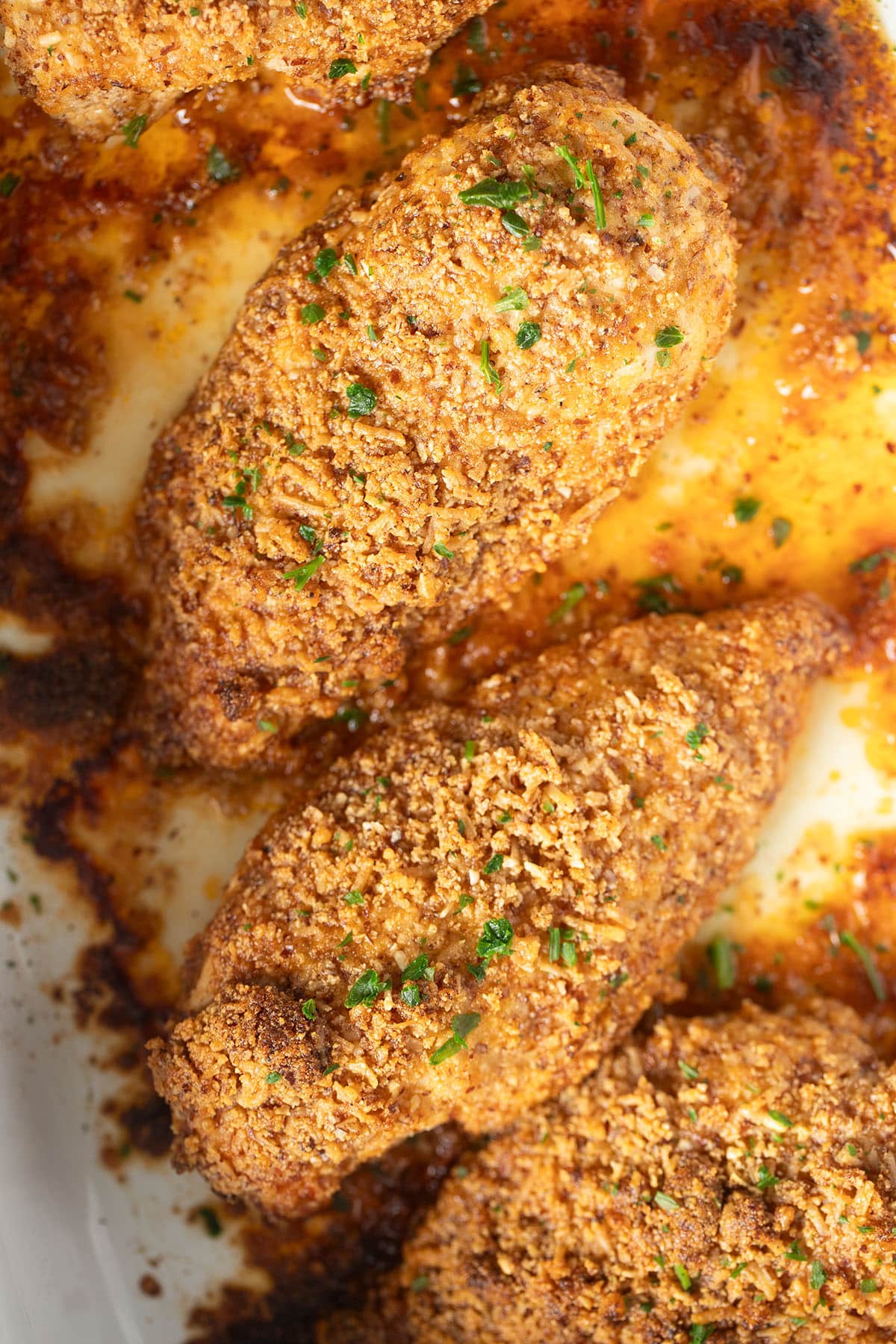 three baked almond crusted chicken breast pieces sprinkled with parsley. 