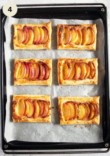 four freshly baked tarts with peaches on a lined baking sheet.