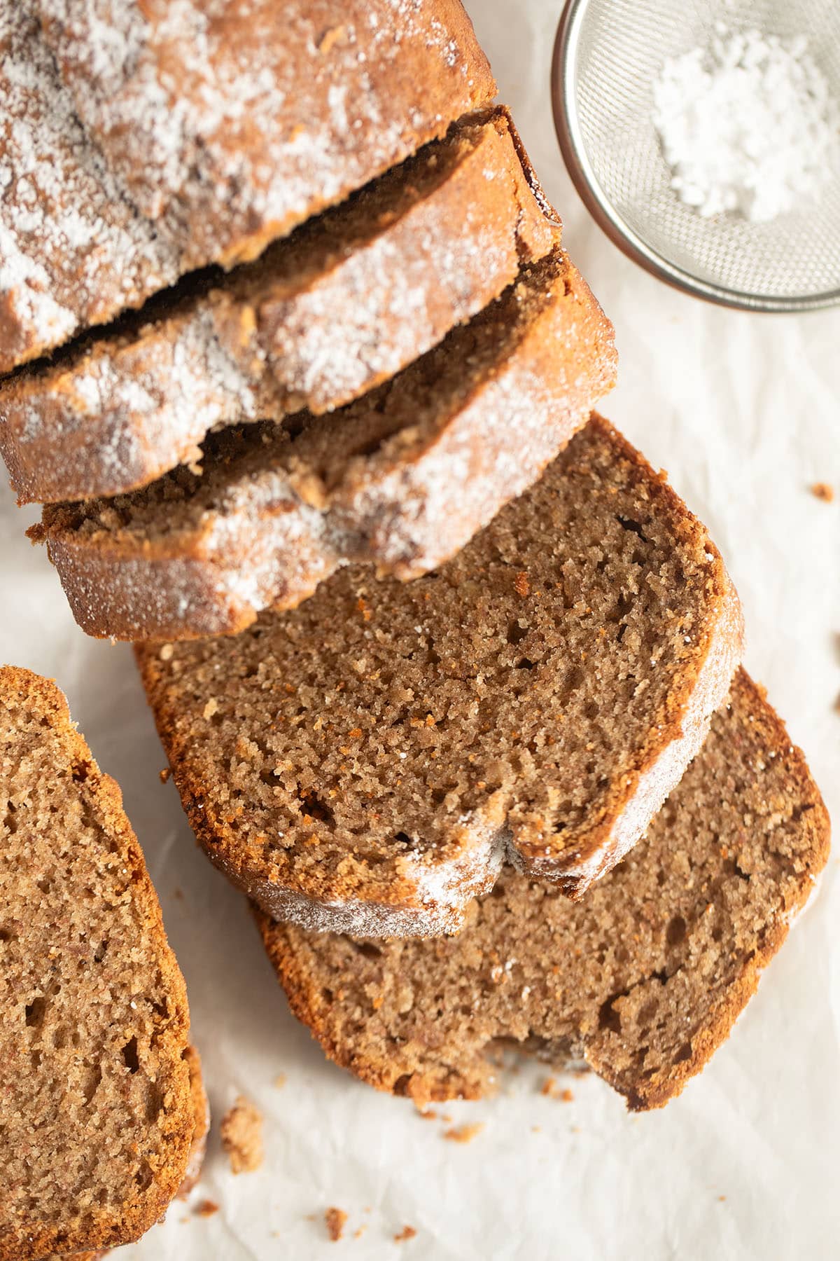 spelt banana bread sliced on the table with a small sieve beside it.