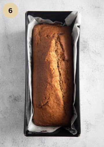 baked banana bread in a loaf pan lined with parchment paper.