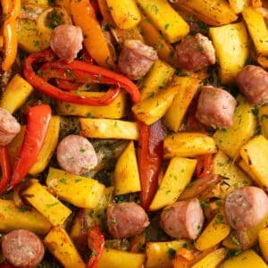 sausage, potatoes, peppers and onions sliced on a baking sheet.