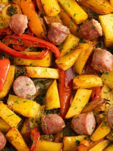 sausage, potatoes, peppers and onions sliced on a baking sheet.