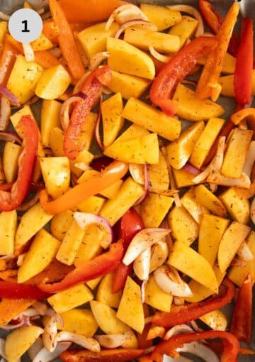 unbaked potato pieces, peppers and onion slices on a baking sheet.