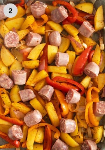 unbaked sausages with potatoes, onions and peppers on a baking tray.