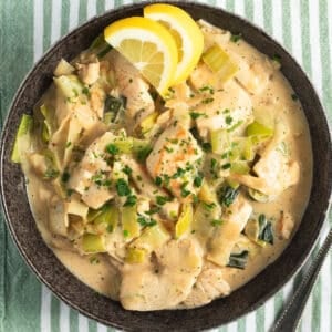 chicken and leeks in a black bowl served with lemon wedges.