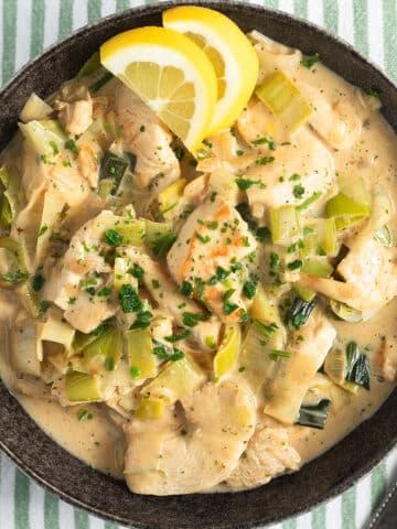 chicken and leeks in a black bowl served with lemon wedges.