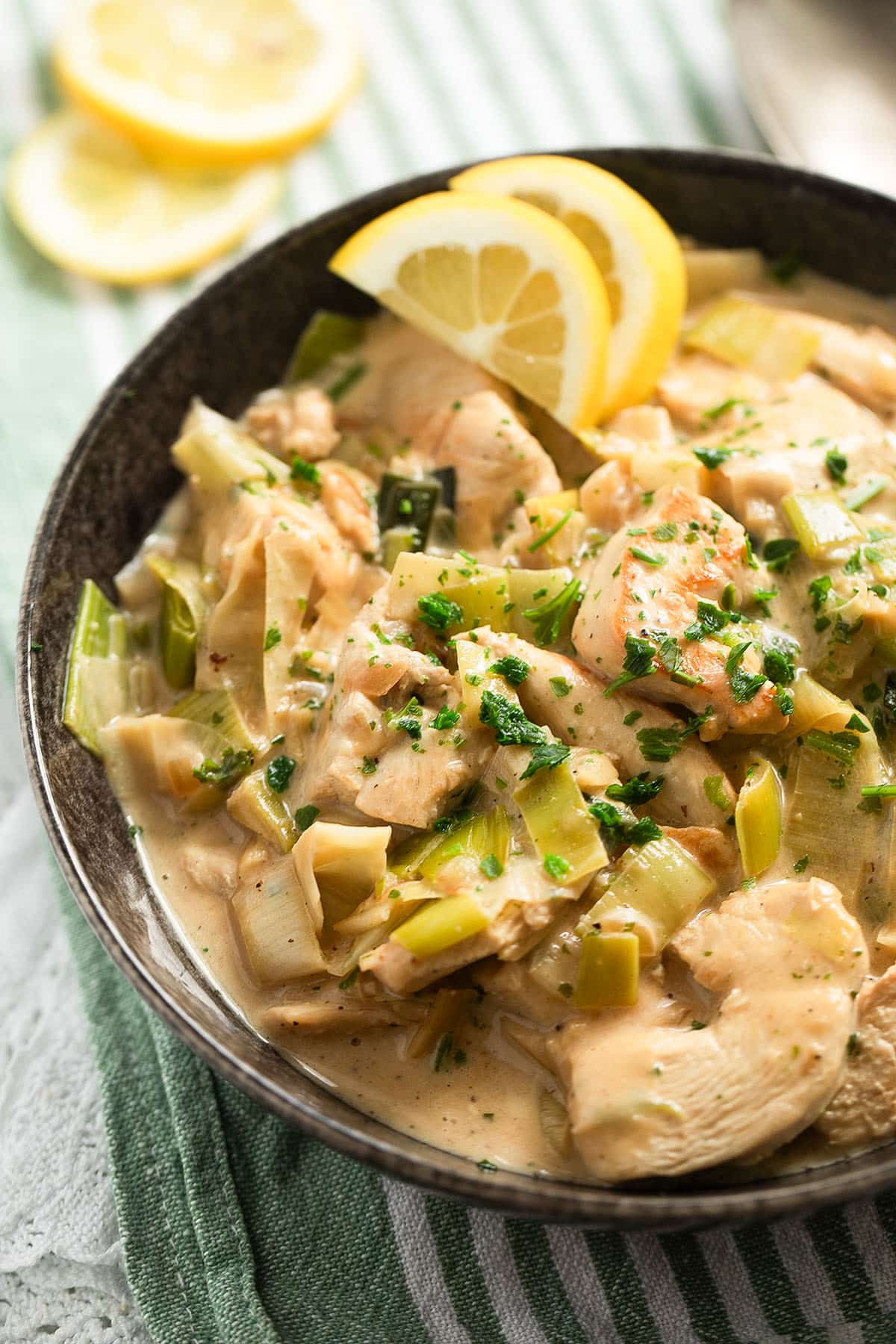 chicken with leeks in a creamy sauce served in a bowl with lemon slices.