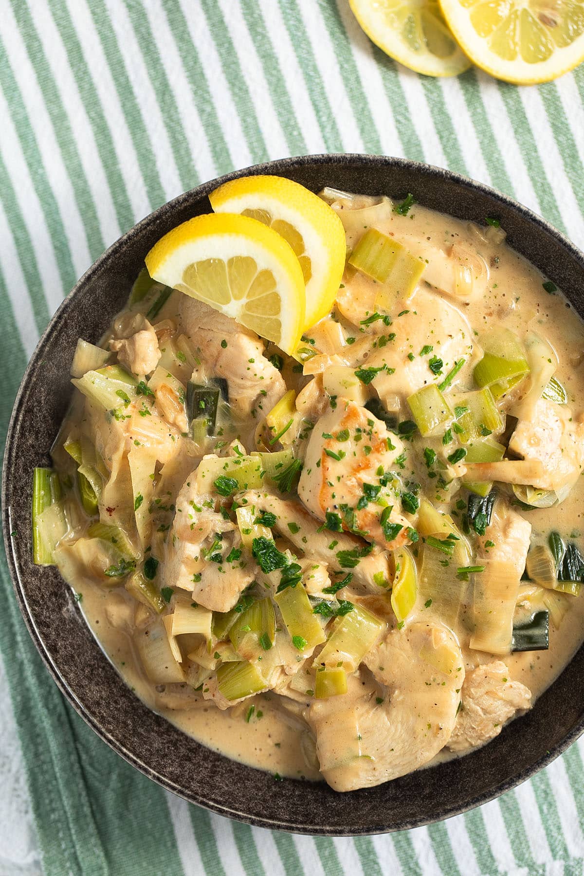 chicken with leeks and creamy sauce in a bowl with lemon wedges.