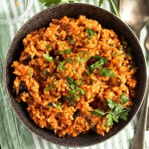 eggplant rice sprinkled with parsley in a dark bowl on a striped kitchen towel.