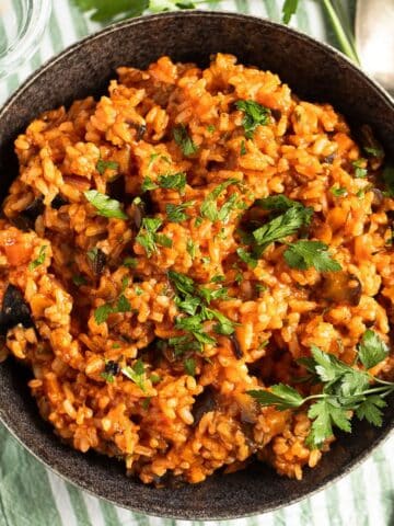 eggplant rice sprinkled with parsley in a dark bowl on a striped kitchen towel.