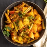 braised green beans potatoes tomatoes sprinkled with parsley in a bowl.