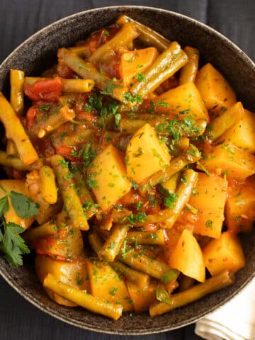 braised green beans potatoes tomatoes sprinkled with parsley in a bowl.