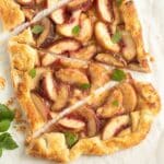 puff pastry peach galette sliced into triangles and decorated with lemon balm leaves.