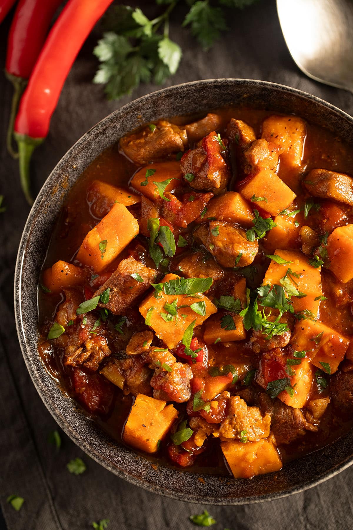 pork stew with sweet potatoes and rich gravy in a bowl, two red chilies on the side.