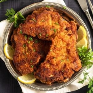 a plate full of turkey schnitzel served with lemon wedges and parsley.