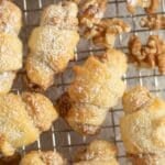 many butterhorn cookies and walnuts halves on a wire rack.