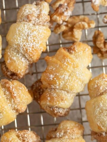 many butterhorn cookies and walnuts halves on a wire rack.