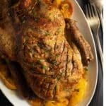 golden and crispy duck in orange sauce on a platter with orange pieces around it.