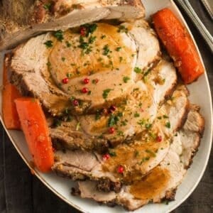 dutch oven pork roast sliced on a platter and served with carrot halves.